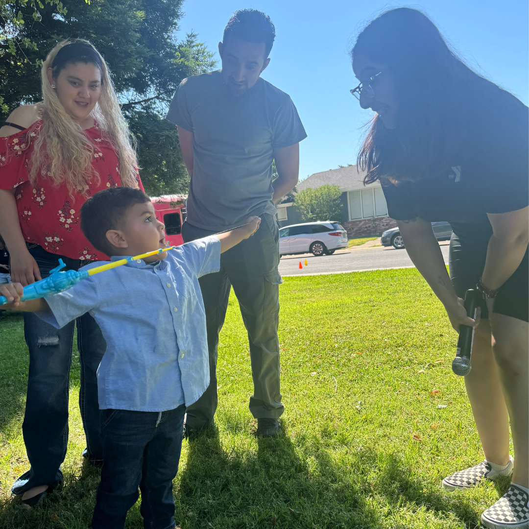 A small child holdings a plastic fishing pole, his parents look at him while he looks up to Stephanie